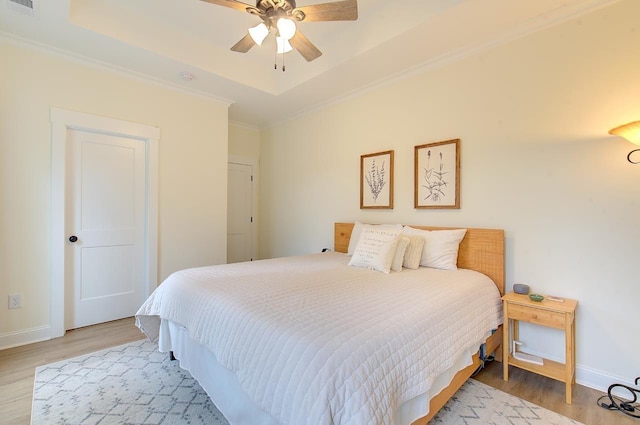 bedroom featuring light wood-type flooring, baseboards, a raised ceiling, and crown molding