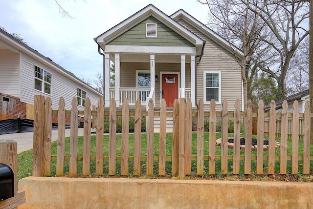 shotgun-style home featuring covered porch and a fenced front yard