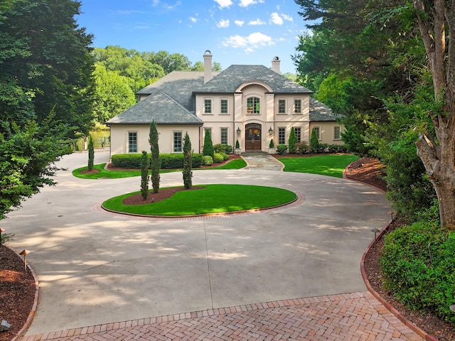 french country home featuring curved driveway, a chimney, a front lawn, and stucco siding