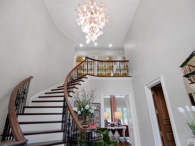 stairway featuring a towering ceiling, a notable chandelier, crown molding, and recessed lighting