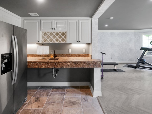 kitchen with a sink, visible vents, white cabinets, baseboards, and stainless steel fridge with ice dispenser