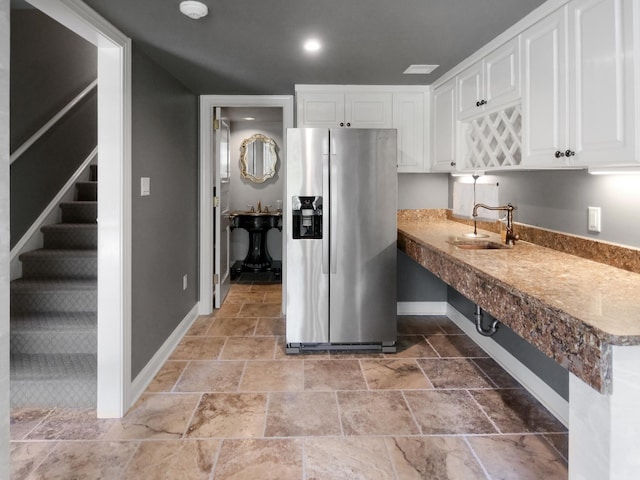 kitchen featuring a sink, white cabinetry, baseboards, stainless steel refrigerator with ice dispenser, and stone finish flooring