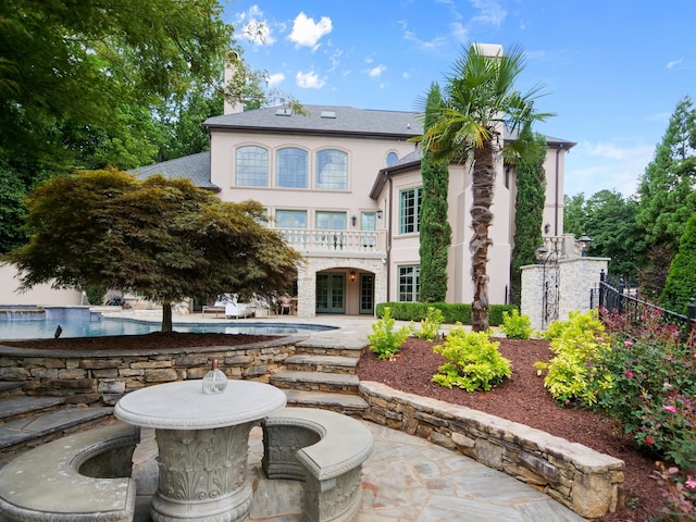 back of property featuring a balcony, an outdoor pool, french doors, stucco siding, and a patio area