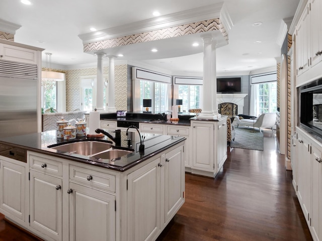 kitchen featuring a fireplace, dark countertops, open floor plan, a sink, and an island with sink