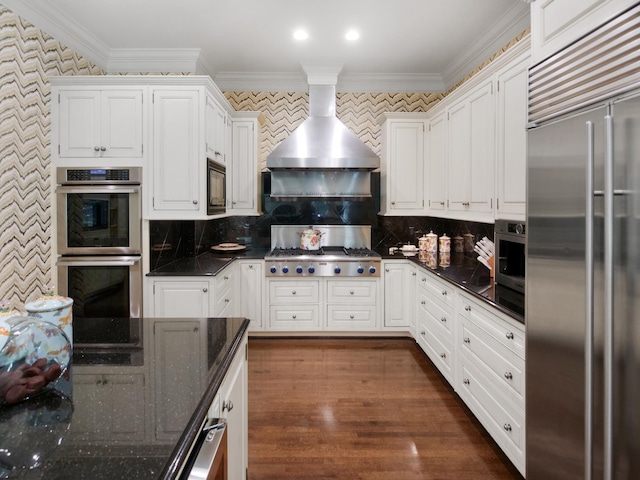 kitchen featuring exhaust hood, white cabinets, crown molding, and built in appliances