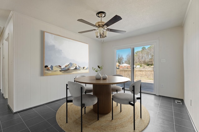 dining area featuring a textured ceiling, ceiling fan, dark tile patterned floors, visible vents, and ornamental molding