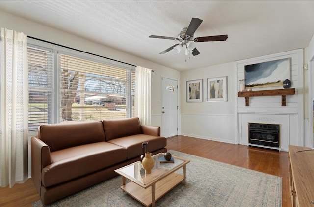 living area with a wainscoted wall, a fireplace, wood finished floors, and a ceiling fan