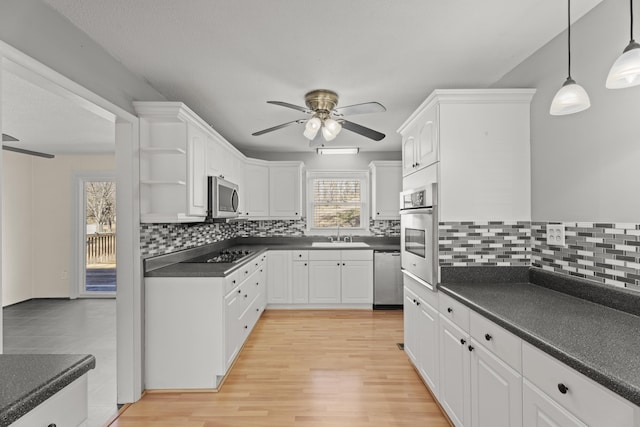 kitchen with white cabinets, dark countertops, appliances with stainless steel finishes, open shelves, and a sink