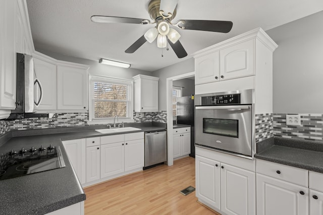 kitchen with dark countertops, white cabinets, stainless steel appliances, and a sink