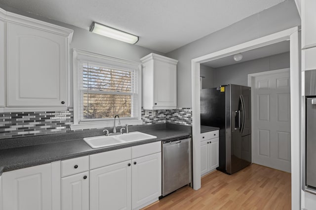 kitchen with stainless steel appliances, dark countertops, backsplash, white cabinets, and a sink