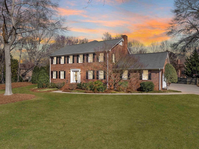 colonial house featuring brick siding, a lawn, and a chimney