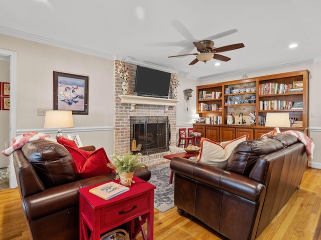 living area featuring light wood finished floors, a brick fireplace, a ceiling fan, and crown molding