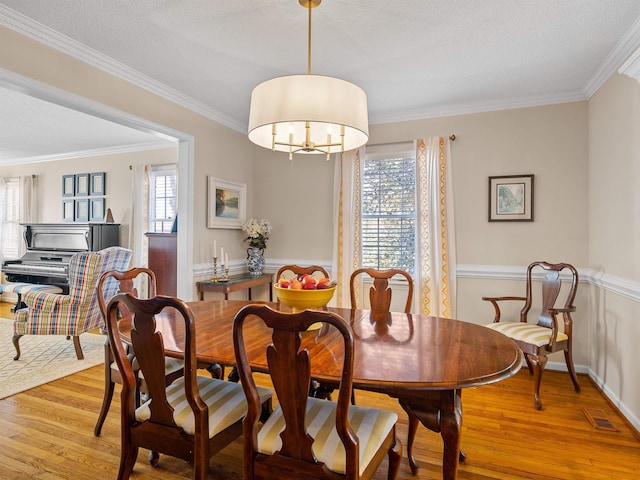 dining room with an inviting chandelier, light wood-style flooring, ornamental molding, and a textured ceiling