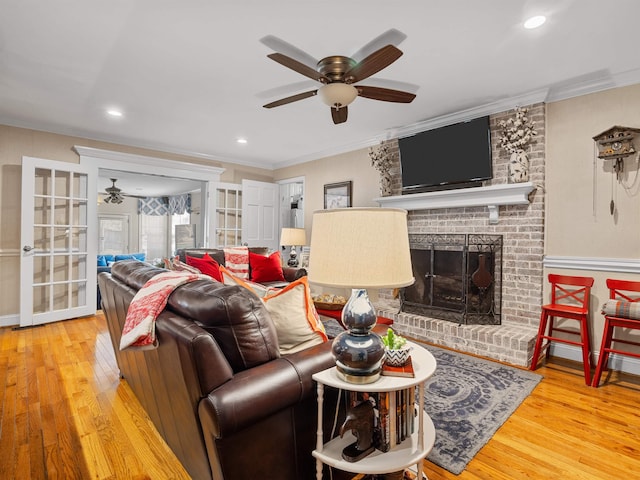 living area with ornamental molding, a fireplace, ceiling fan, and wood finished floors