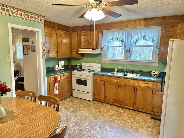 kitchen featuring brown cabinets, dark countertops, a sink, white appliances, and under cabinet range hood