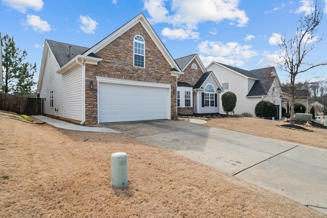 traditional-style house with driveway, stone siding, an attached garage, and fence