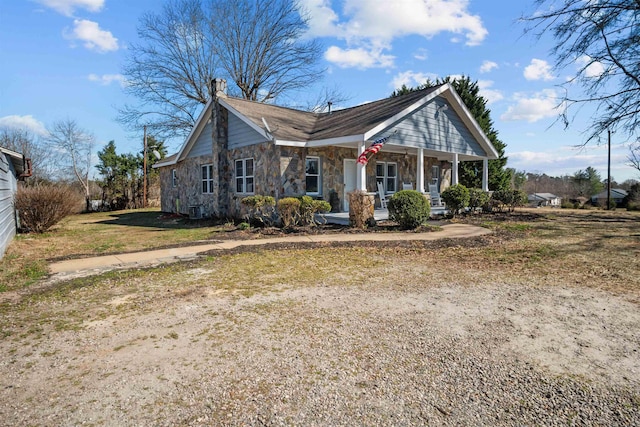 view of front of home with stone siding, a chimney, and covered porch