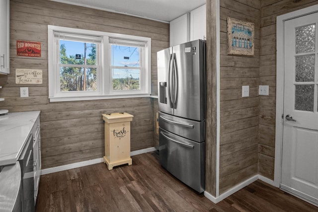 kitchen with dark wood-style floors, stainless steel fridge with ice dispenser, white cabinets, wood walls, and baseboards