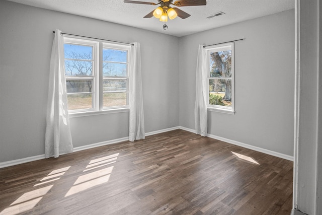 unfurnished room with a textured ceiling, wood finished floors, visible vents, and baseboards