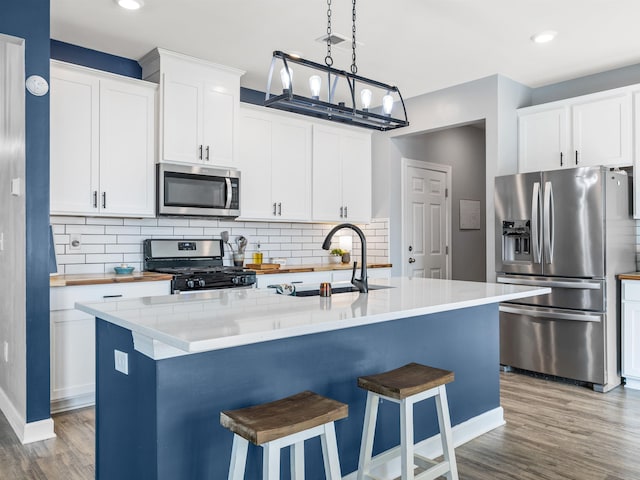 kitchen featuring stainless steel appliances, a kitchen island with sink, a sink, and wood finished floors