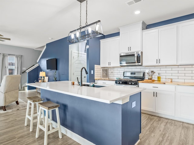 kitchen with decorative backsplash, appliances with stainless steel finishes, light wood-style floors, open floor plan, and a sink