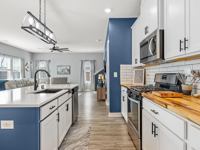 kitchen featuring stainless steel appliances, decorative backsplash, open floor plan, a sink, and butcher block countertops