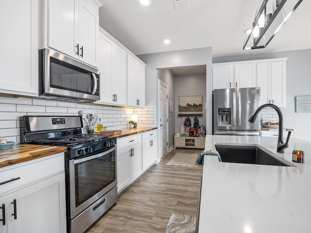 kitchen featuring light wood finished floors, butcher block countertops, appliances with stainless steel finishes, white cabinetry, and a sink