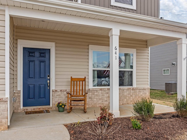 property entrance featuring covered porch, central AC, brick siding, and board and batten siding