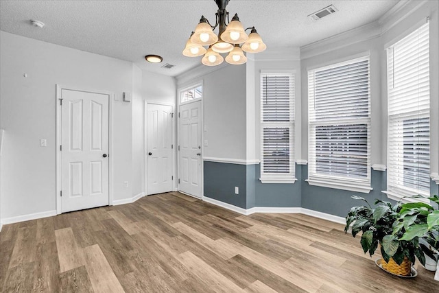 empty room featuring a textured ceiling, wood finished floors, visible vents, and a chandelier