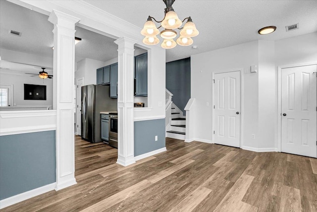 unfurnished dining area with ceiling fan with notable chandelier, wood finished floors, ornate columns, and stairs