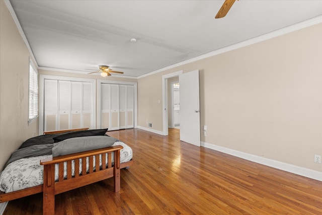 bedroom featuring crown molding, multiple closets, ceiling fan, wood finished floors, and baseboards