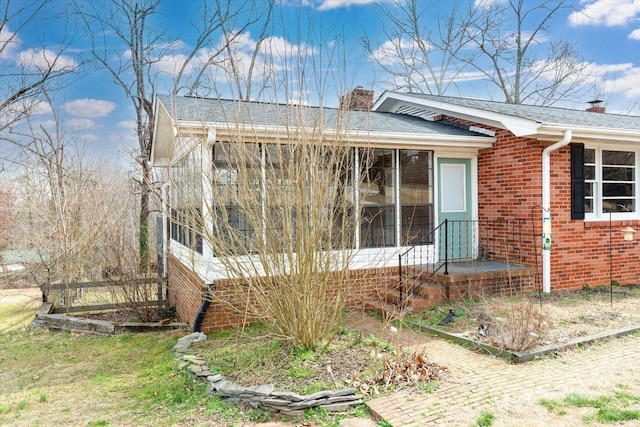 view of side of home featuring a sunroom, a chimney, and brick siding