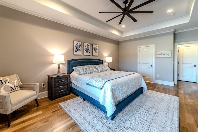 bedroom with light wood finished floors, a tray ceiling, ornamental molding, and baseboards