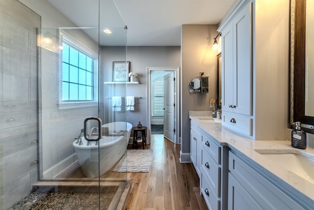 full bathroom with a sink, double vanity, a soaking tub, and wood finished floors