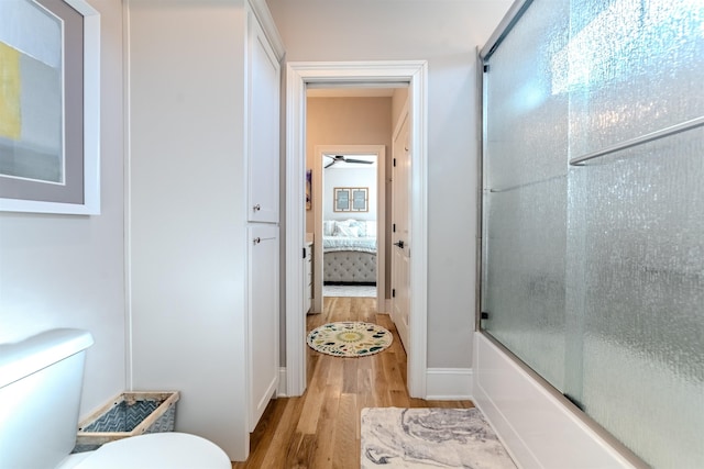 ensuite bathroom with connected bathroom, toilet, ceiling fan, wood finished floors, and combined bath / shower with glass door