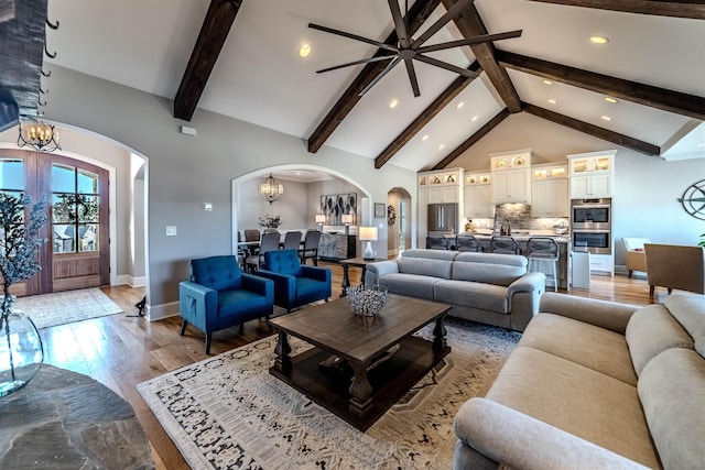 living area featuring an inviting chandelier, arched walkways, light wood finished floors, and high vaulted ceiling