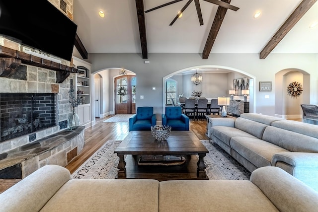 living room featuring arched walkways, a fireplace, wood finished floors, baseboards, and beamed ceiling