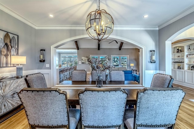 dining space with arched walkways, wood finished floors, an inviting chandelier, crown molding, and built in shelves