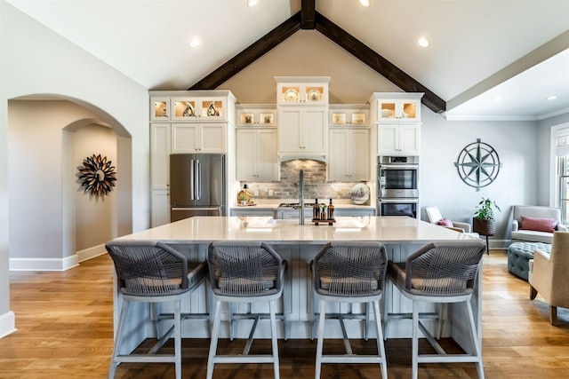 kitchen featuring arched walkways, a large island, light wood-style flooring, lofted ceiling with beams, and appliances with stainless steel finishes