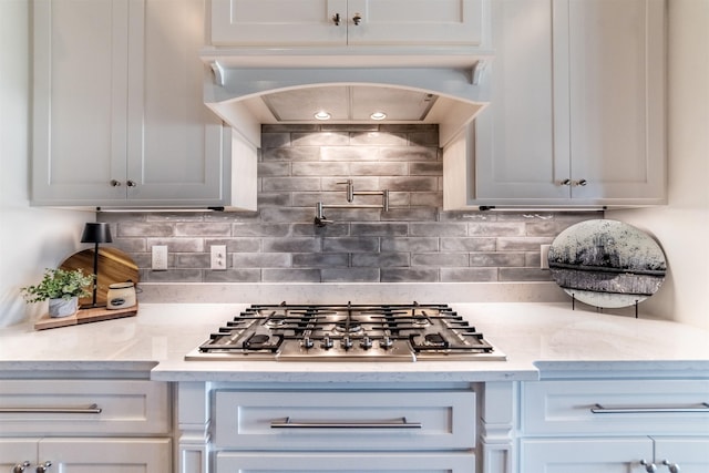 kitchen with tasteful backsplash, custom exhaust hood, light stone counters, and stainless steel gas stovetop