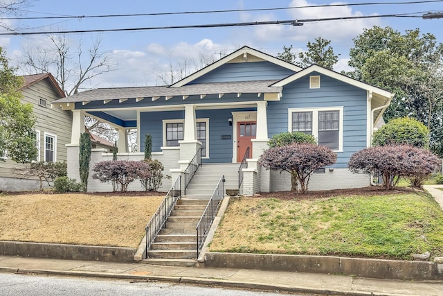 view of front of property with covered porch, stairway, roof with shingles, and a front yard