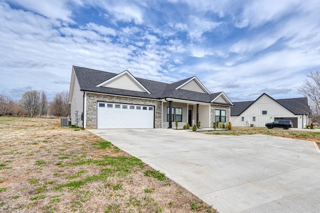 view of front of property featuring an attached garage, central AC, a shingled roof, concrete driveway, and stone siding