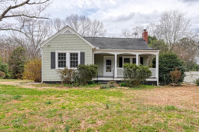 view of front of home featuring covered porch, a shingled roof, a chimney, and a front yard