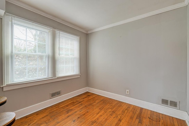 empty room featuring hardwood / wood-style floors, baseboards, visible vents, and crown molding