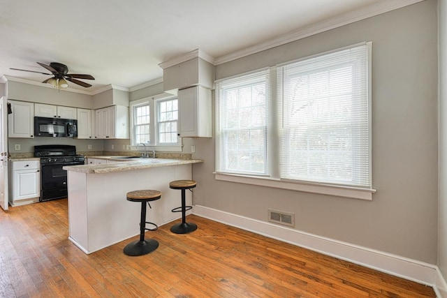 kitchen with visible vents, light wood-style flooring, a sink, a peninsula, and black appliances