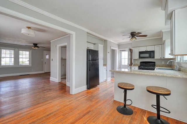 kitchen with crown molding, black appliances, a peninsula, and light wood-style floors