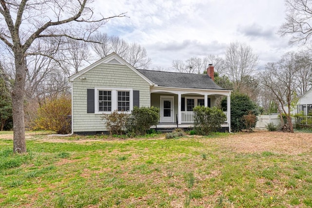 view of front of house featuring covered porch, a front lawn, a chimney, and fence