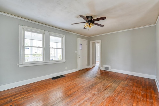 empty room with wood-type flooring, visible vents, crown molding, and baseboards