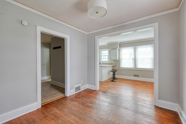 spare room featuring crown molding, visible vents, baseboards, and hardwood / wood-style floors