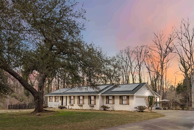 ranch-style home featuring concrete driveway, a front yard, roof mounted solar panels, fence, and a garage